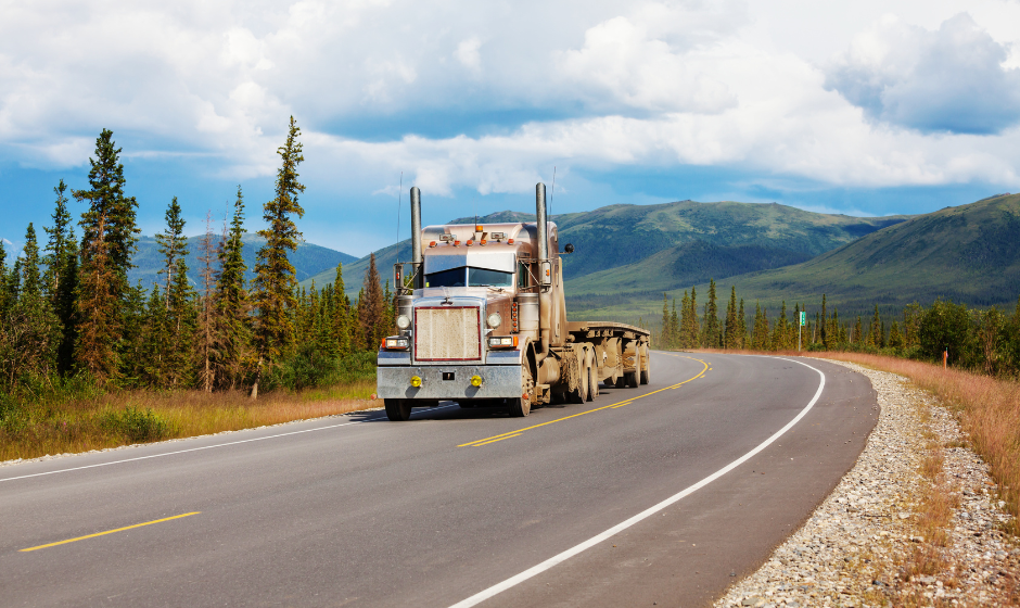 A semi with flatbed trailer travel a highway through Alaska