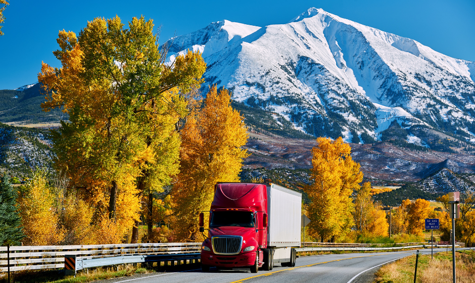 A semi truck travels on a highway with a mountain in the background