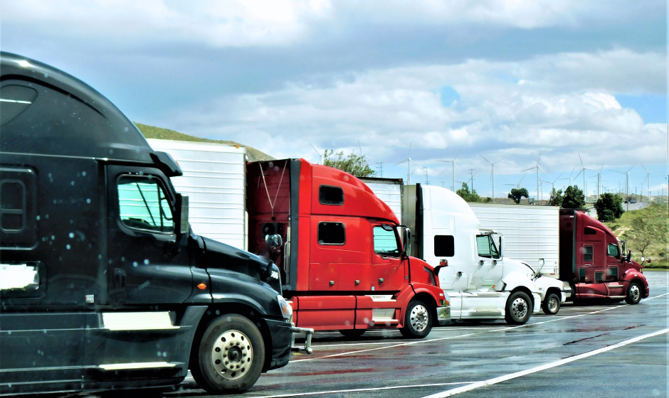 A line of trucks with dry van trailers parked at a truck stop