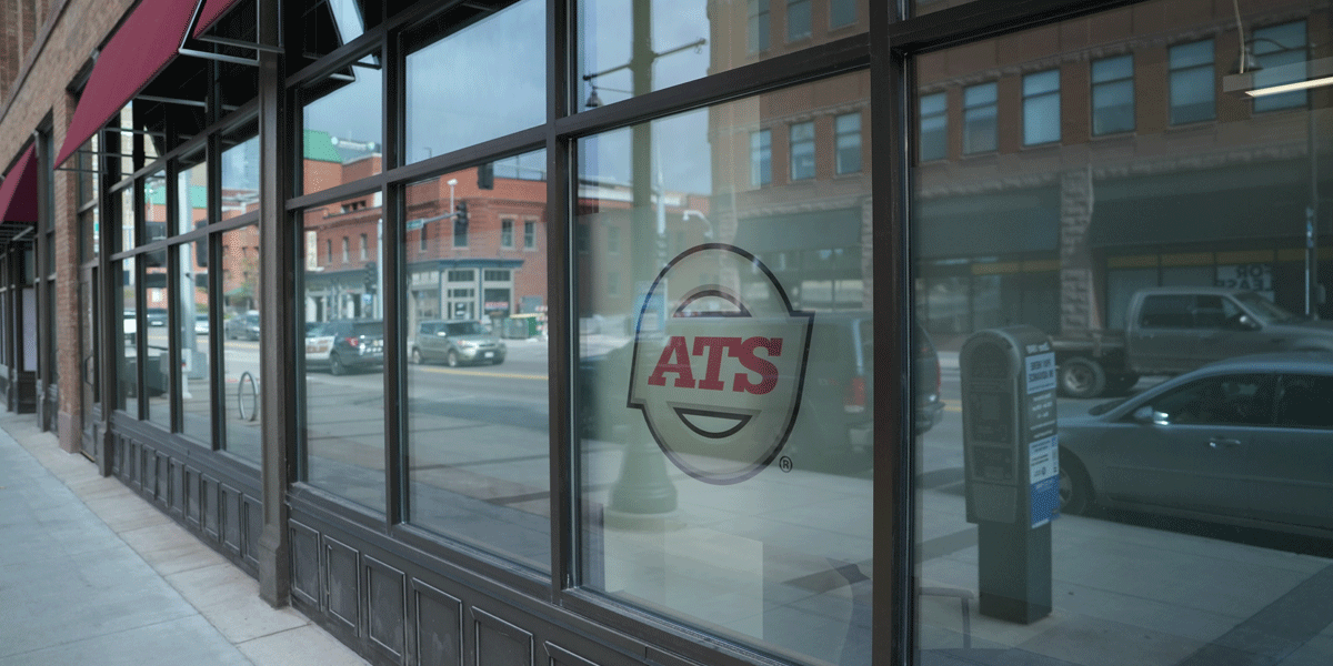 ATS logo on a window. The reflection of businesses across the street can be seen in the windows.