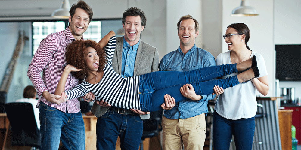 Four people standing in a line and holding a woman. They all wear work attire.