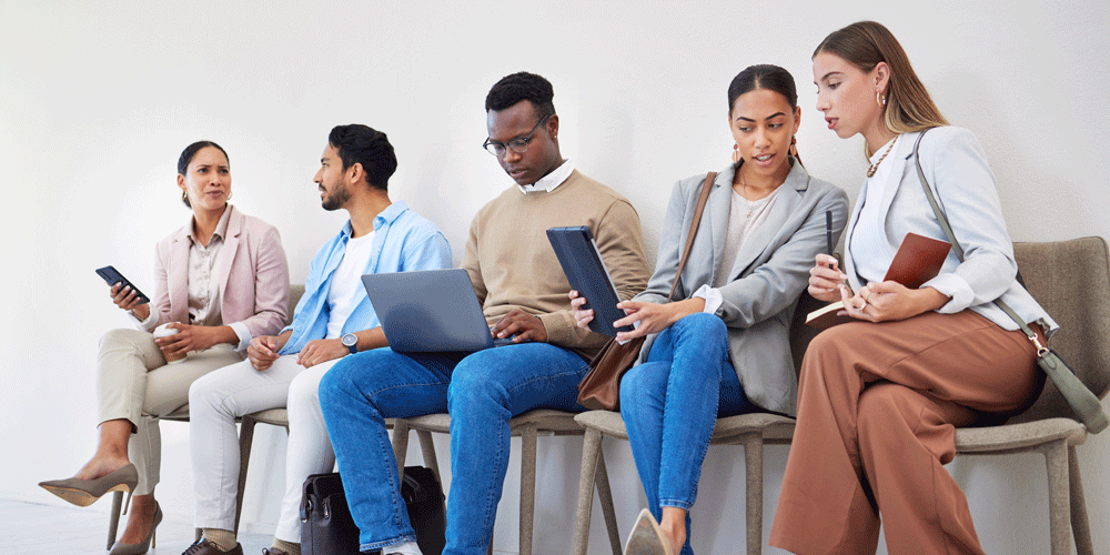 A line of people in business casual clothing waiting in chairs to be interviewed.