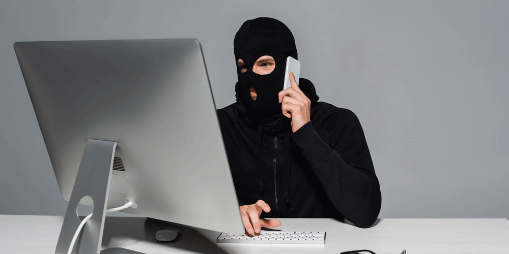 Hacker in all black and a balaclava behind a computer screen.  