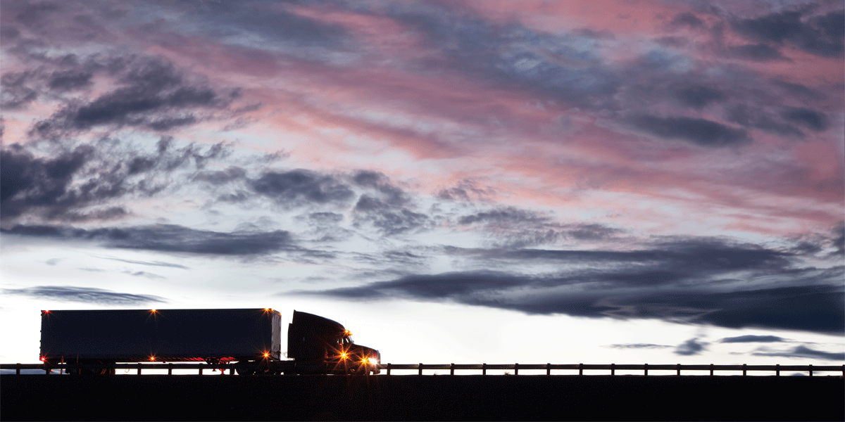 Semi-truck with dry van trailer in the distance at dusk. The sky is cloudy.