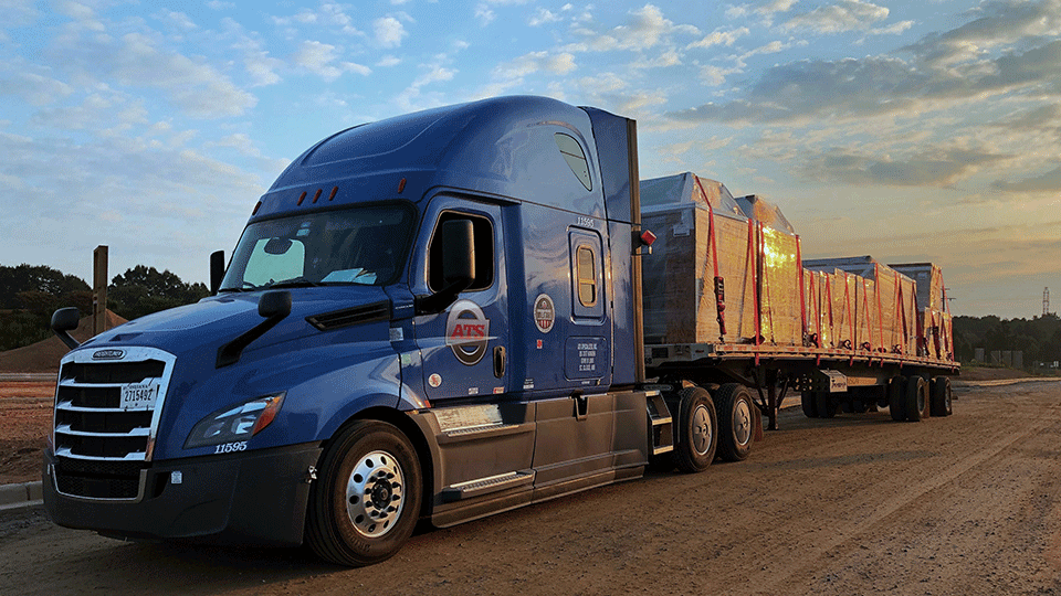 A semi truck and flatbed trailer with shrink-wrapped freight.