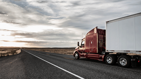 Red semi truck heading into sunset on highway